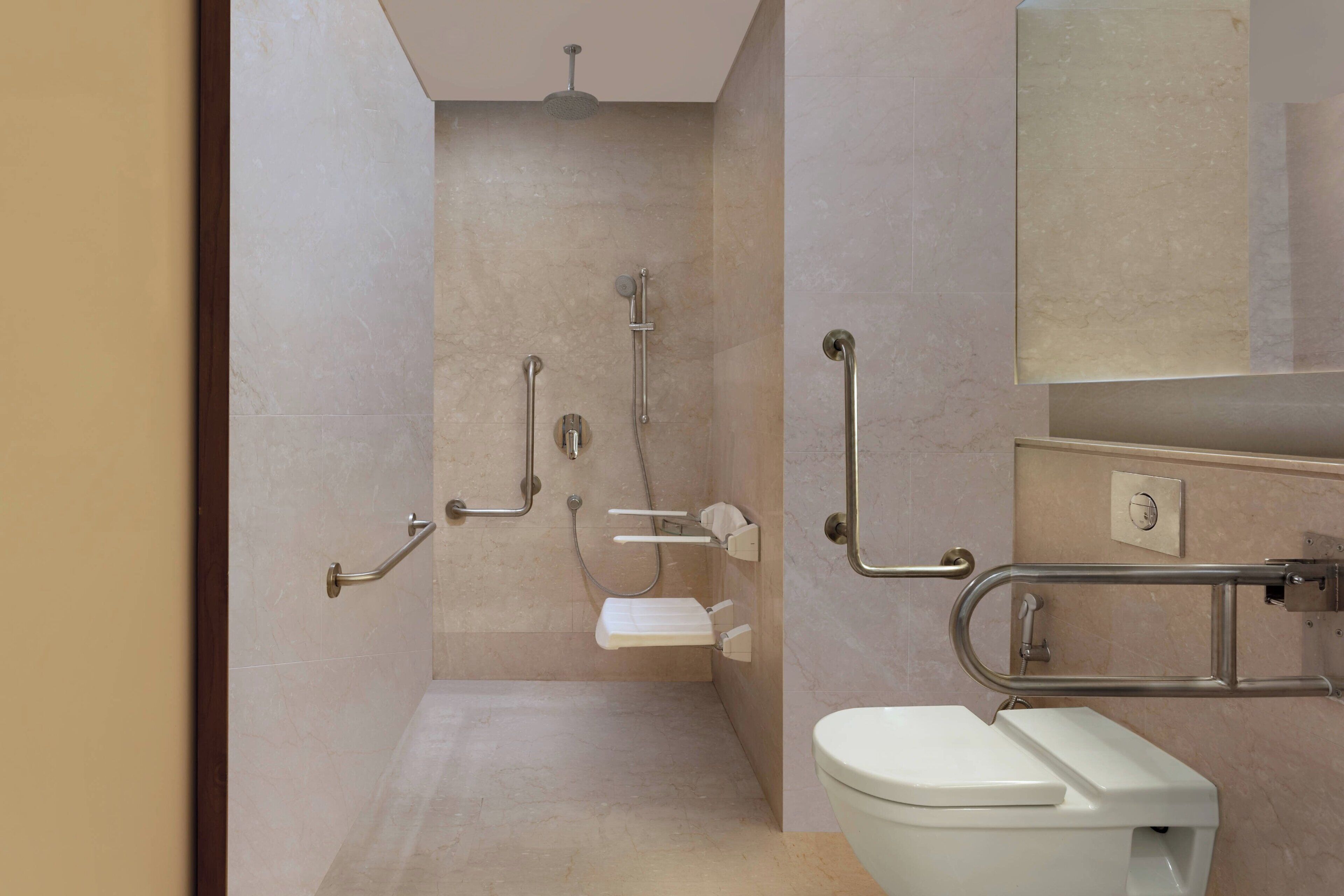 A modern bathroom with a toilet, grab bars, a shower with a handheld showerhead, and a wall-mounted toilet paper holder.