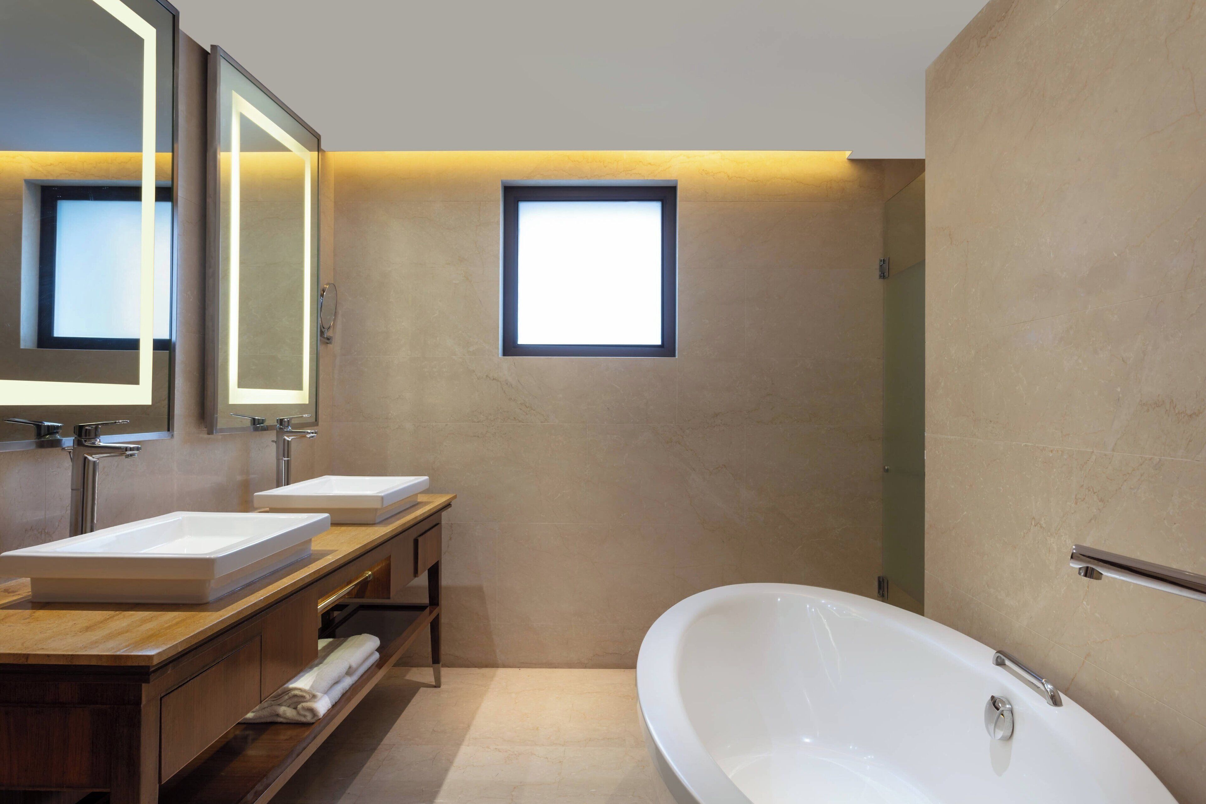 Un baño moderno con dos lavamanos, una bañera grande y una ventana pequeña.