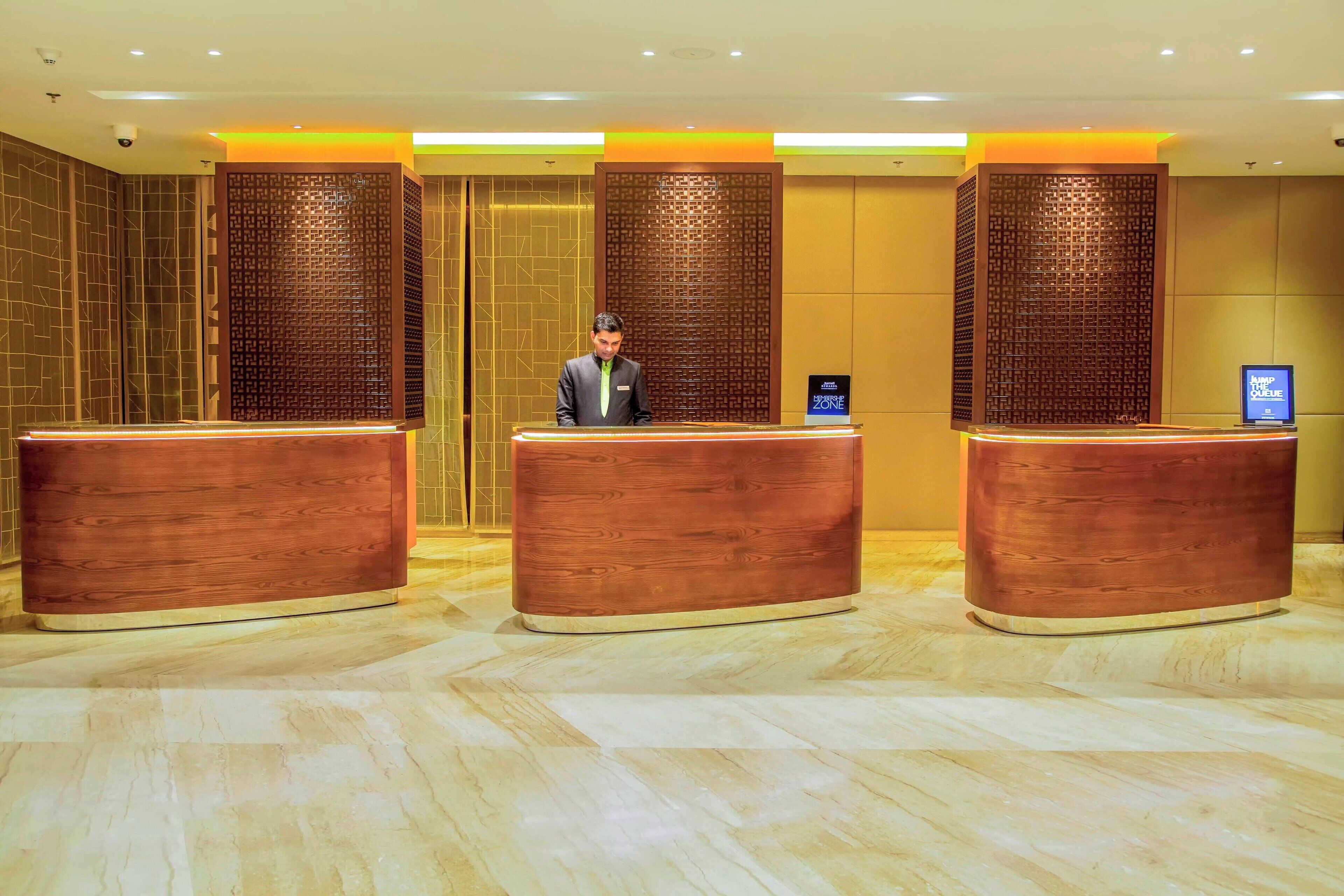 A hotel reception area with three wooden reception desks, a security camera, and a digital display.