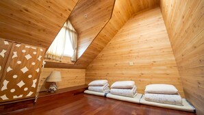 A wooden cabin with a sloped ceiling, a bed with pillows, a lamp, and a patterned cabinet. - SongYuan Hotel (Lugu)