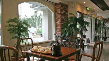 A dining area with a table set for two, surrounded by chairs, with a view of the outdoors through large windows.