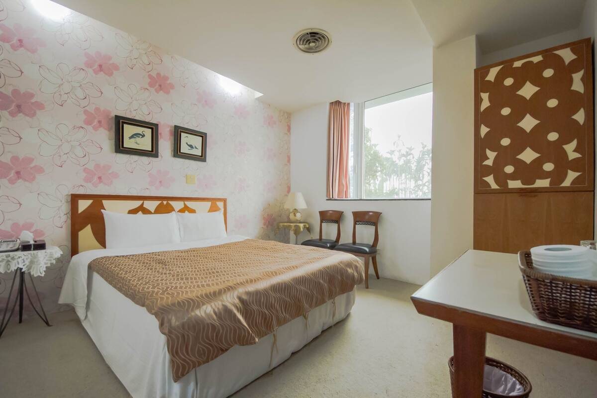 A hotel room with a bed, two chairs, a table, a lamp, and a window with curtains.