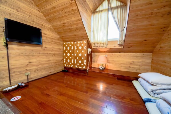 A wooden-paneled room with a flat-screen TV mounted on the wall, a bed with pillows, a bedside table with a lamp, and a patterned cabinet. - SongYuan Hotel (Lugu)