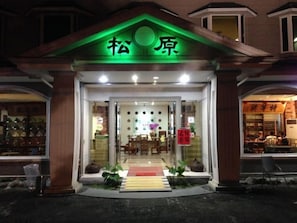 A building with a green-lit entrance and a sign above it. Inside, there are tables and chairs arranged for dining. - SongYuan Hotel (Lugu)