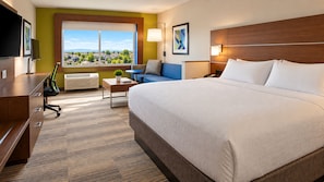 A hotel room with a large bed, a desk, a chair, a small table, a lamp, a TV, and a window with a view of houses. - Holiday Inn Express & Suites Boise Airport by IHG (Boise)