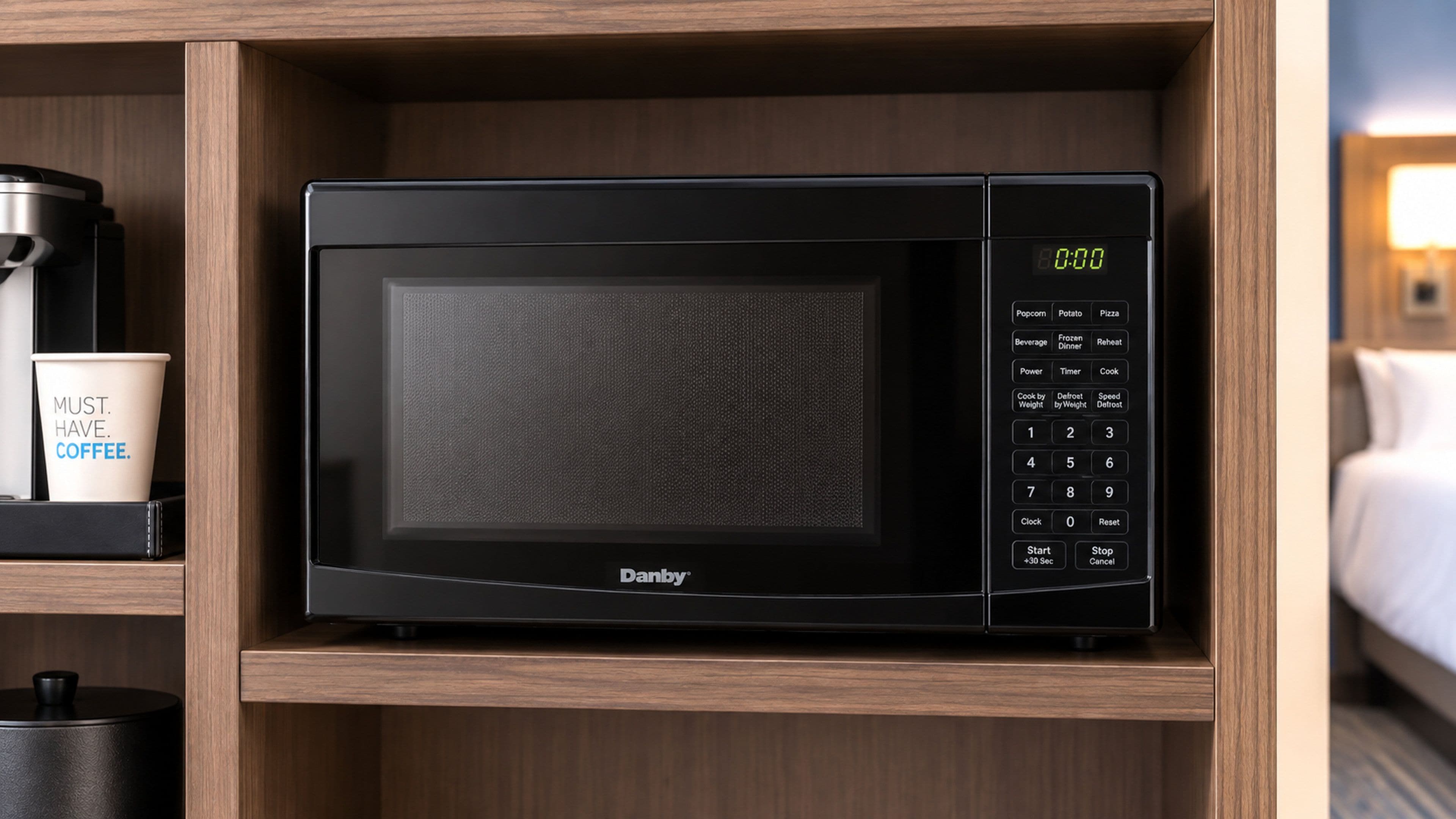 A black microwave oven with a digital display, control panel, and brand name 'Danby' on a wooden shelf.