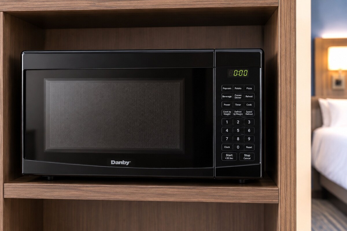 A black microwave oven with a digital display, control panel, and brand name 'Danby' on a wooden shelf.