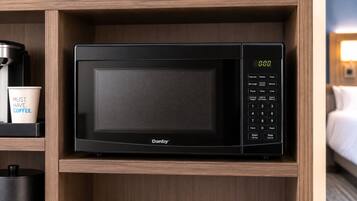 A black microwave oven with a digital display, control panel, and brand name 'Danby' on a wooden shelf.