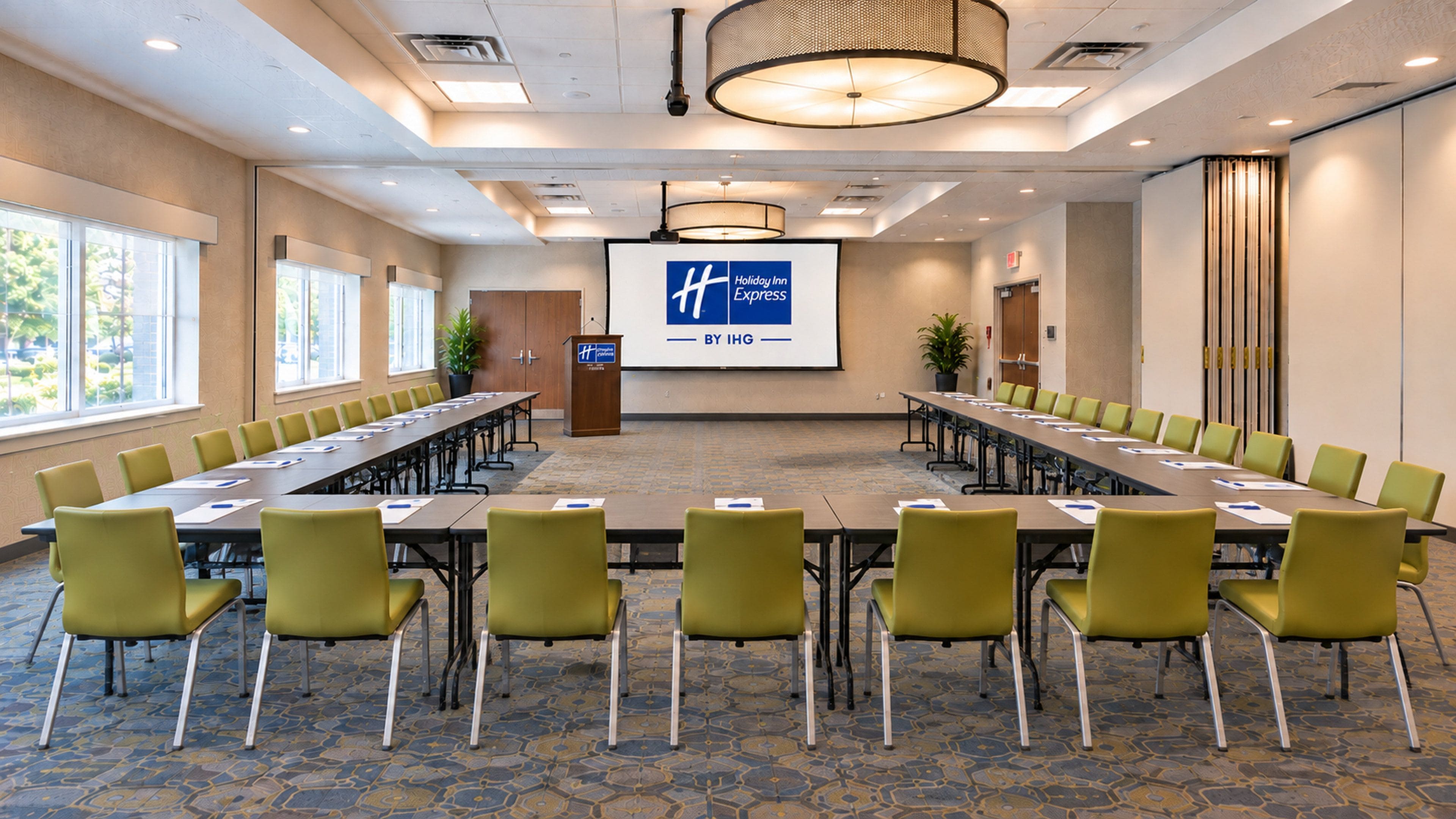 A conference room with a long table, multiple chairs, a projector screen, and a podium.