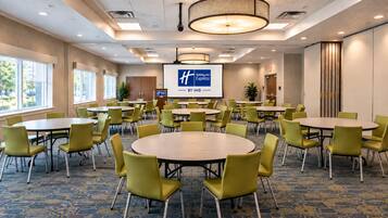 Un salón de conferencias con varias mesas y sillas, una pantalla de proyector y el logotipo de Holiday Inn Express.