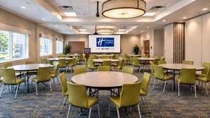 A conference room with multiple tables and chairs, a projector screen, and a Holiday Inn Express logo. - Holiday Inn Express & Suites Boise Airport by IHG (Boise)
