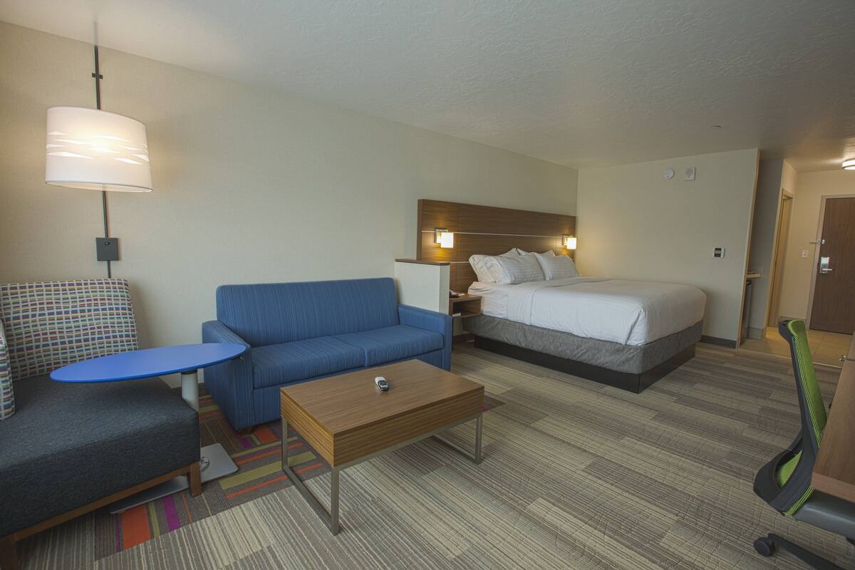 A hotel room with a bed, a blue sofa, a small table, a lamp, and a chair.