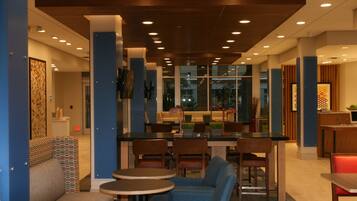 A modern hotel lobby with a bar area, seating arrangements, and a view through large windows.