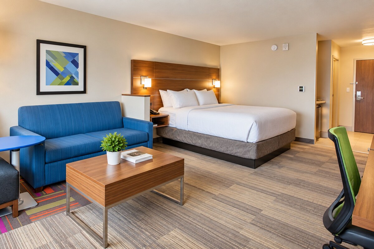 A hotel room with a bed, a sofa, a desk, a chair, a lamp, and a framed picture on the wall.