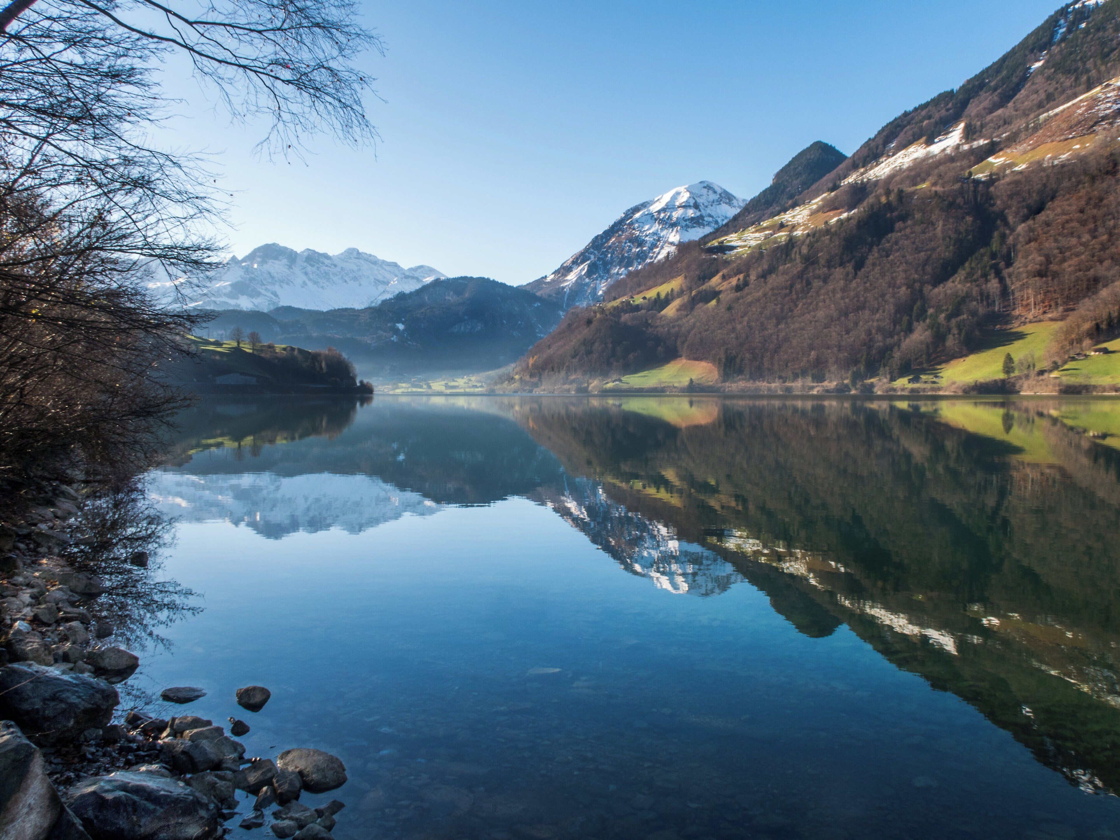 A calm lake with clear reflections, surrounded by mountains and trees.