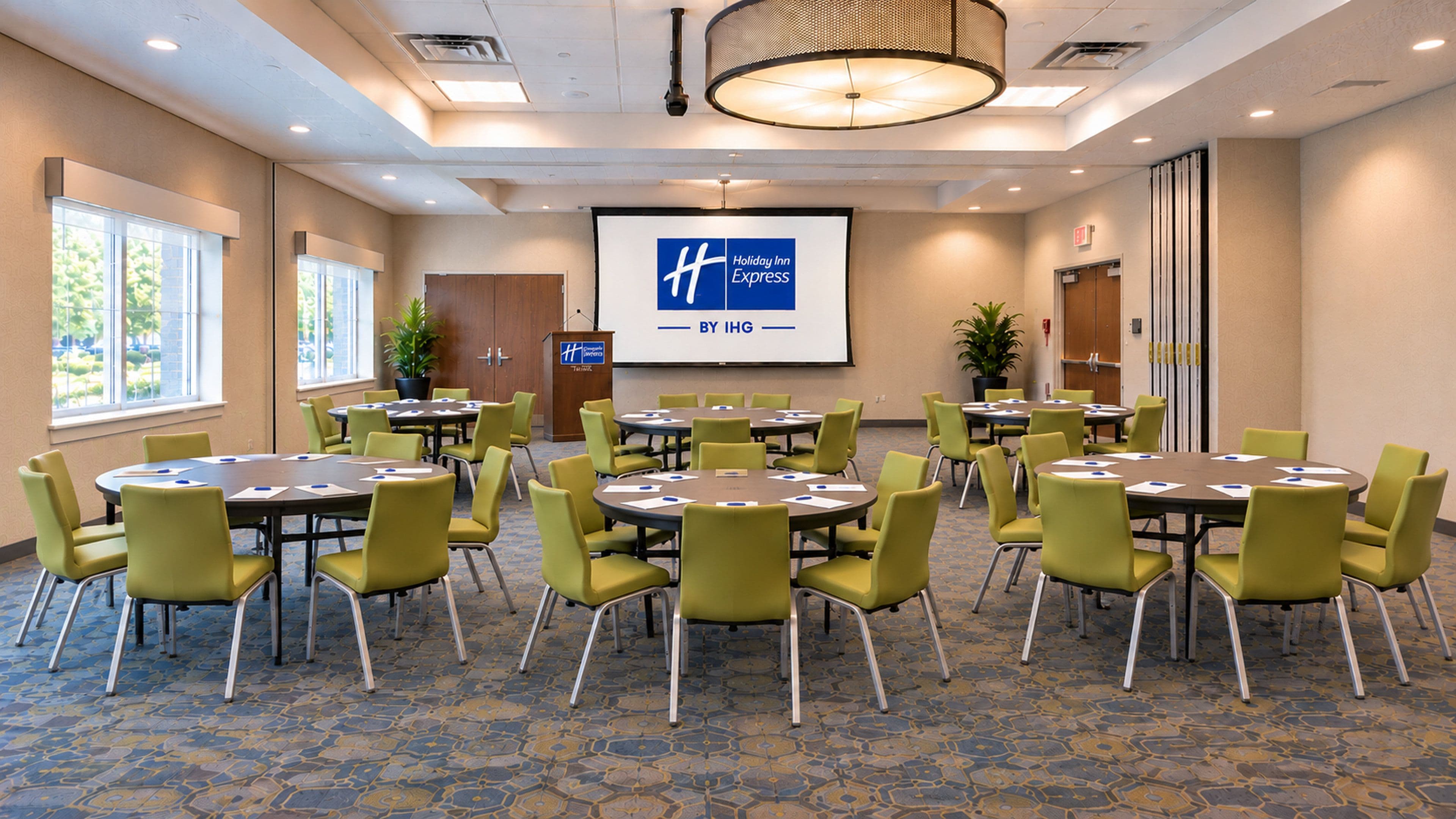 A conference room with multiple tables and chairs, a projector screen, and a podium.