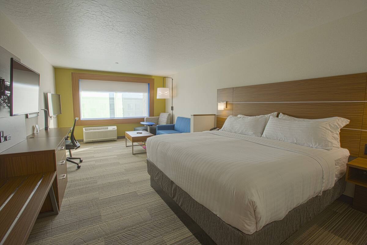A hotel room with a large bed, a desk, a chair, a window, and a radiator.