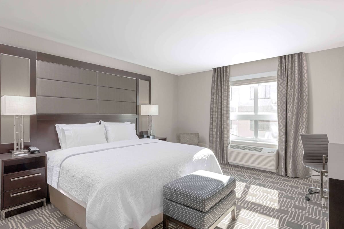 Une chambre d’hôtel avec un grand lit, des lampes de chevet, une fenêtre avec des rideaux, une chaise et une petite table.