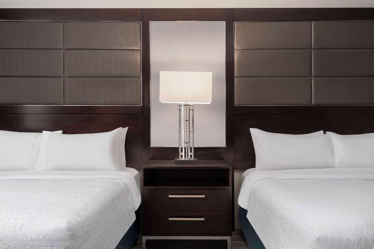Une chambre d’hôtel avec deux lits, une table de chevet avec une lampe et un grand miroir au mur.