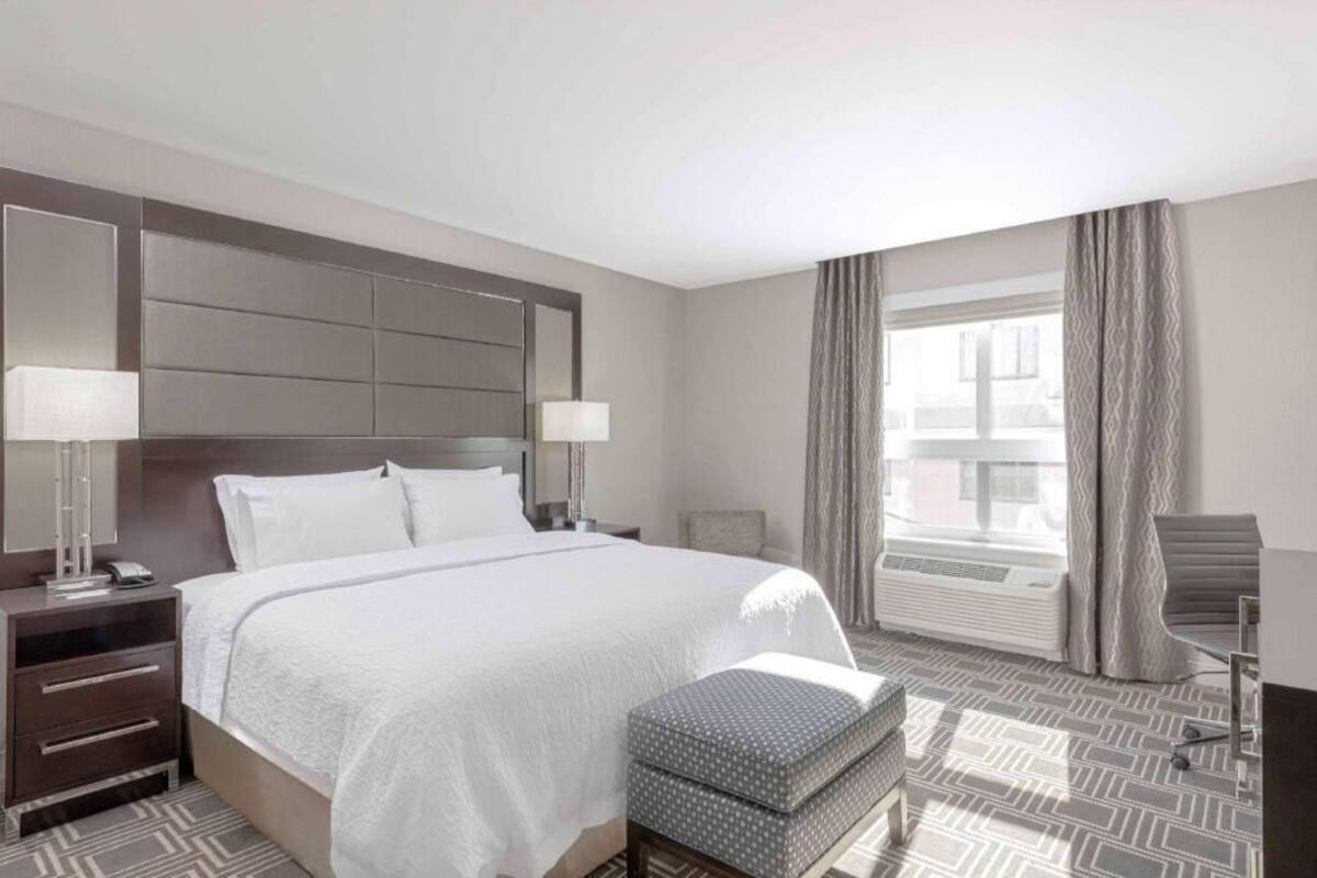 Une chambre d’hôtel avec un grand lit, des tables de chevet, un bureau, une chaise et une fenêtre avec des rideaux.