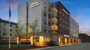 Un hotel Hampton Inn & Suites con diseño moderno, que destaca un letrero llamativo y una entrada bien iluminada.