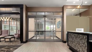 Zona de recepción de un hotel con puerta de vidrio, área de estar con sillas y mostrador de recepción.