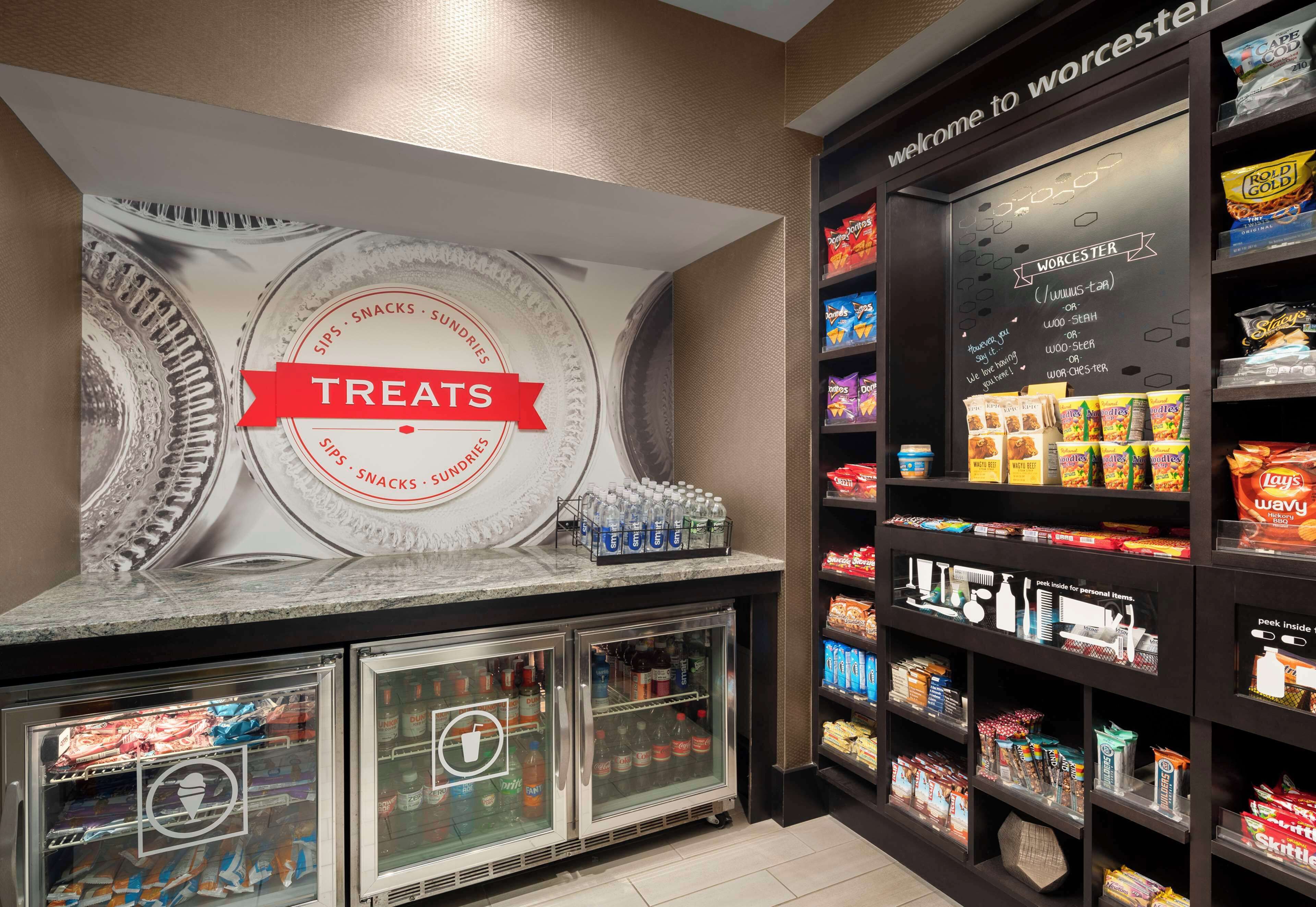 A snack bar with a 'Treats' sign, refrigerated drink dispensers, and shelves stocked with various snacks and beverages.