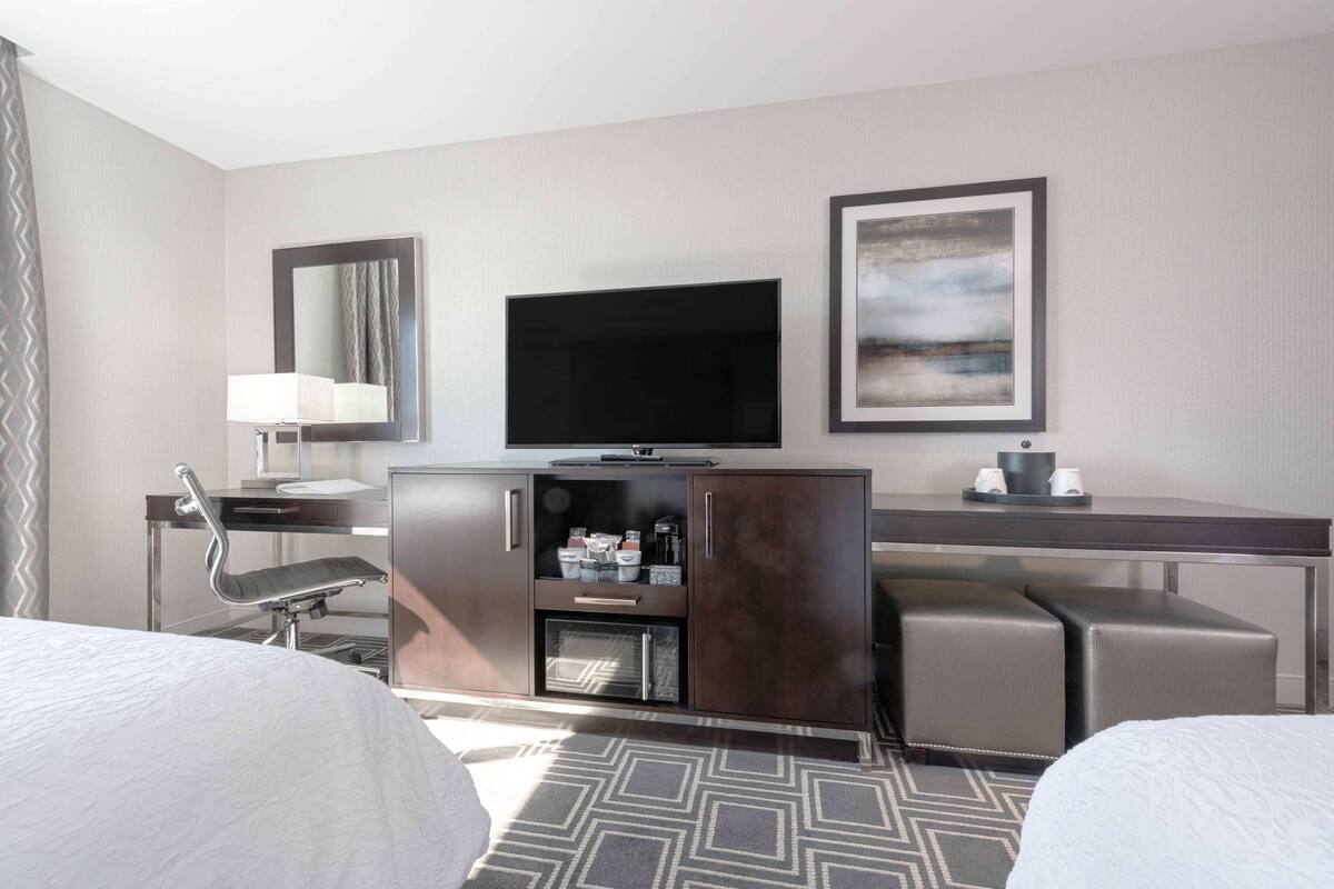 Une chambre d’hôtel comprenant un lit, un bureau avec une chaise, une télévision, une armoire et un tableau encadré accroché au mur.