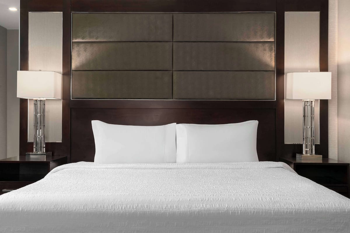 Une chambre d’hôtel avec un grand lit, deux lampes de chevet, une tête de lit en bois foncé et un grand miroir au-dessus du lit.