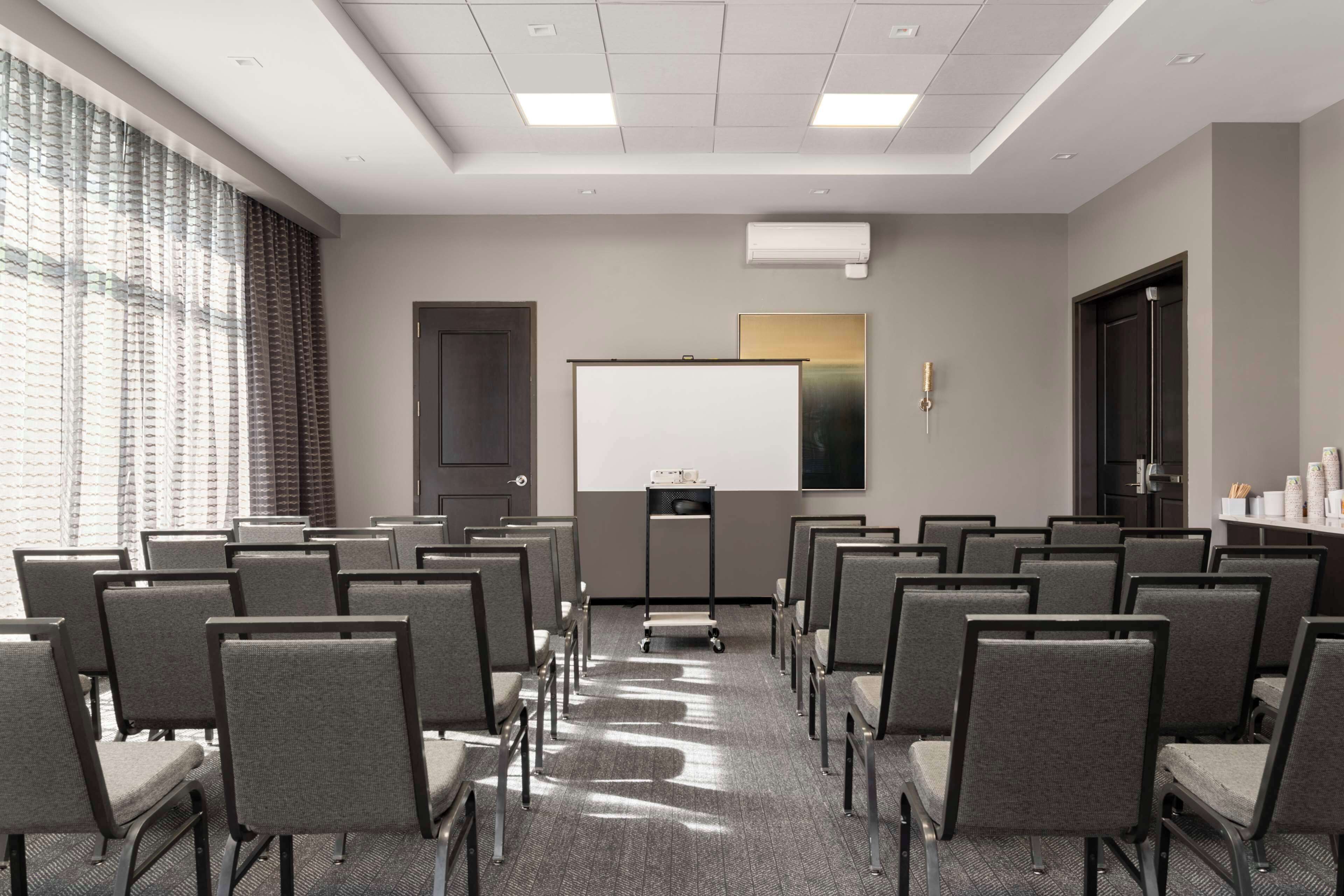 Un salón de conferencias con filas de sillas, una pizarra y una pantalla para proyector.