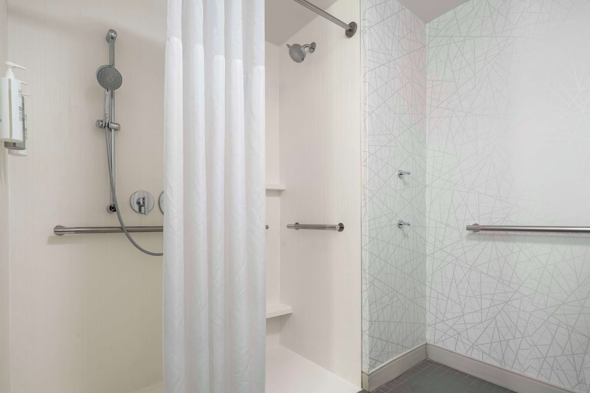 Une salle de bain moderne dotée d’une cabine de douche en verre, d’un pommeau de douche à main et d’un porte-serviettes.
