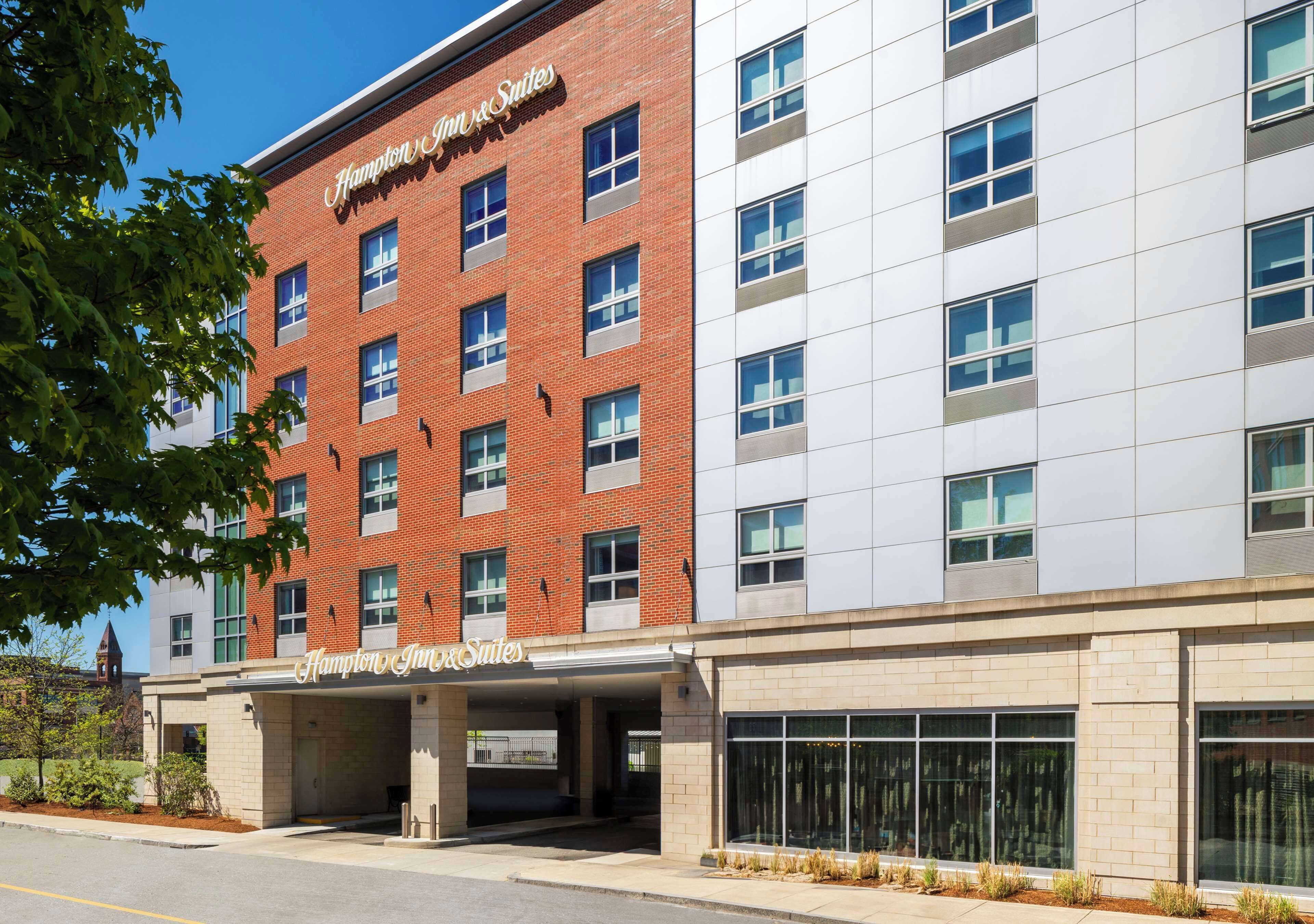 Un hôtel Hampton Inn & Suites à la façade en briques, doté de grandes fenêtres et d’une entrée abritée.