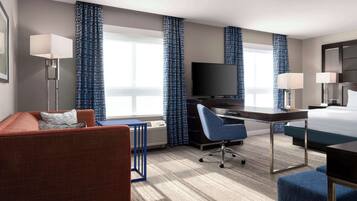 Een hotelkamer met een bed, bureau, stoel, bank, televisie en gordijnen.