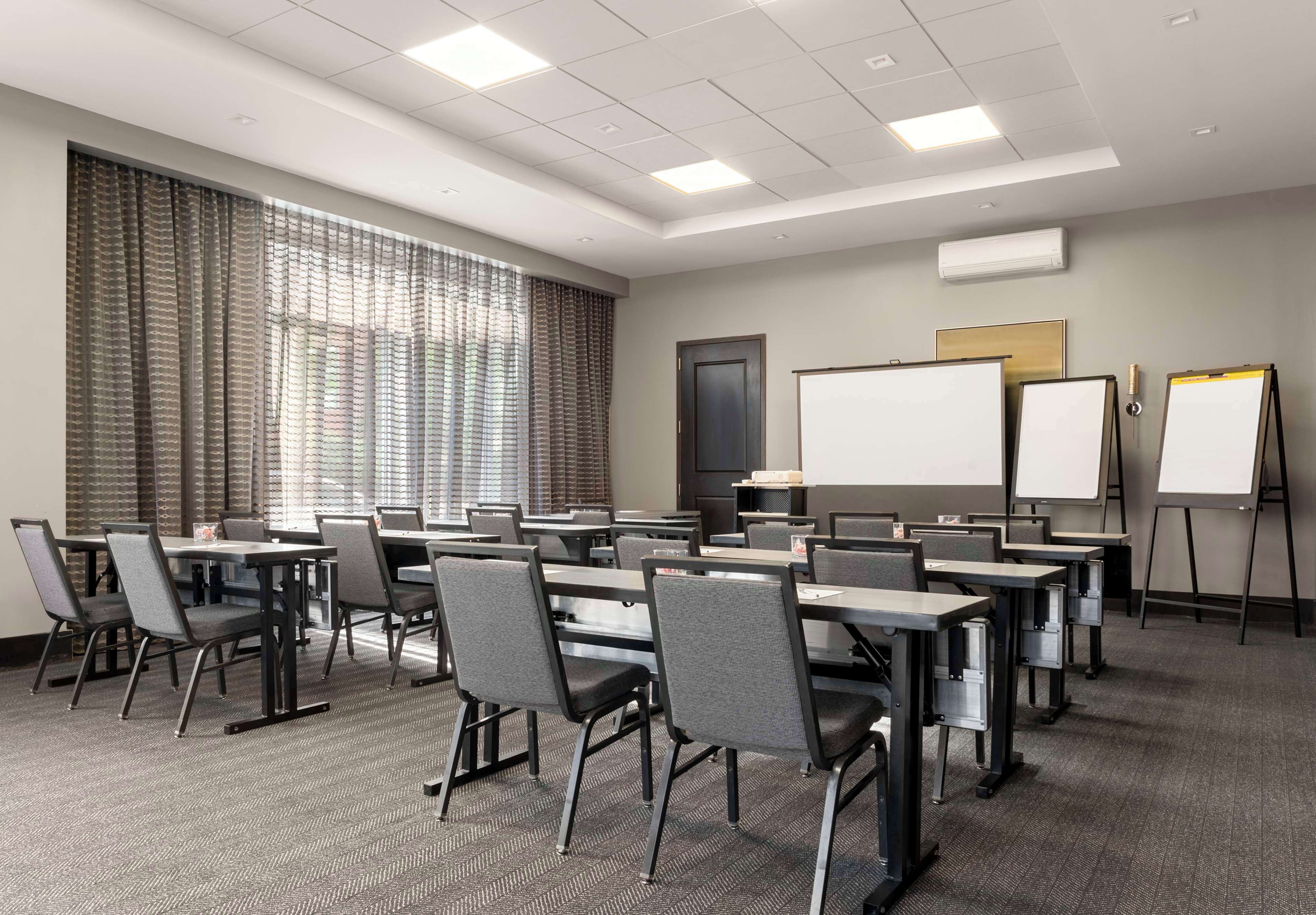 A conference room with multiple tables and chairs, a whiteboard, and a projector screen.