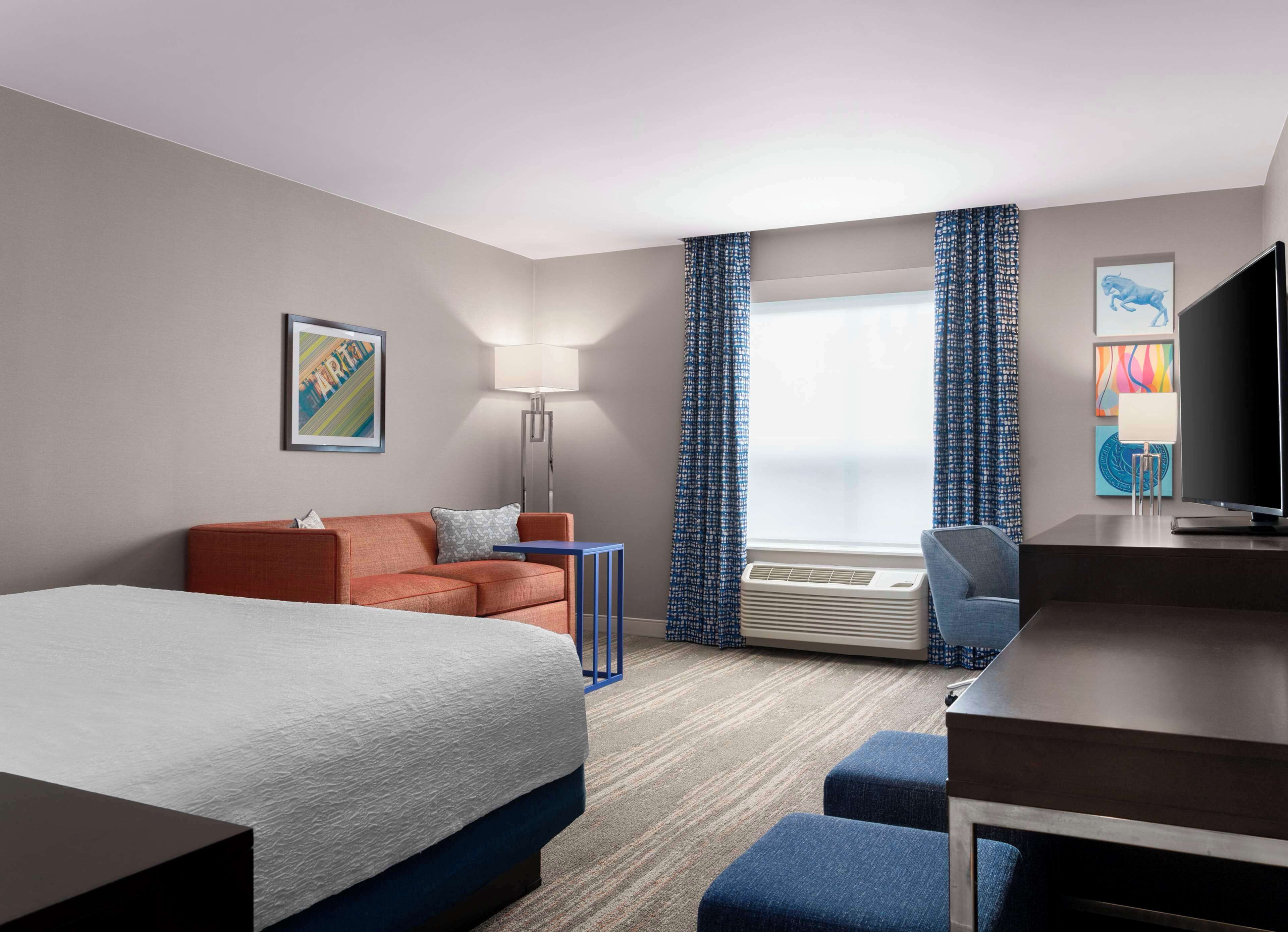 A hotel room with a bed, a sofa, a desk, a chair, a lamp, and a TV.
