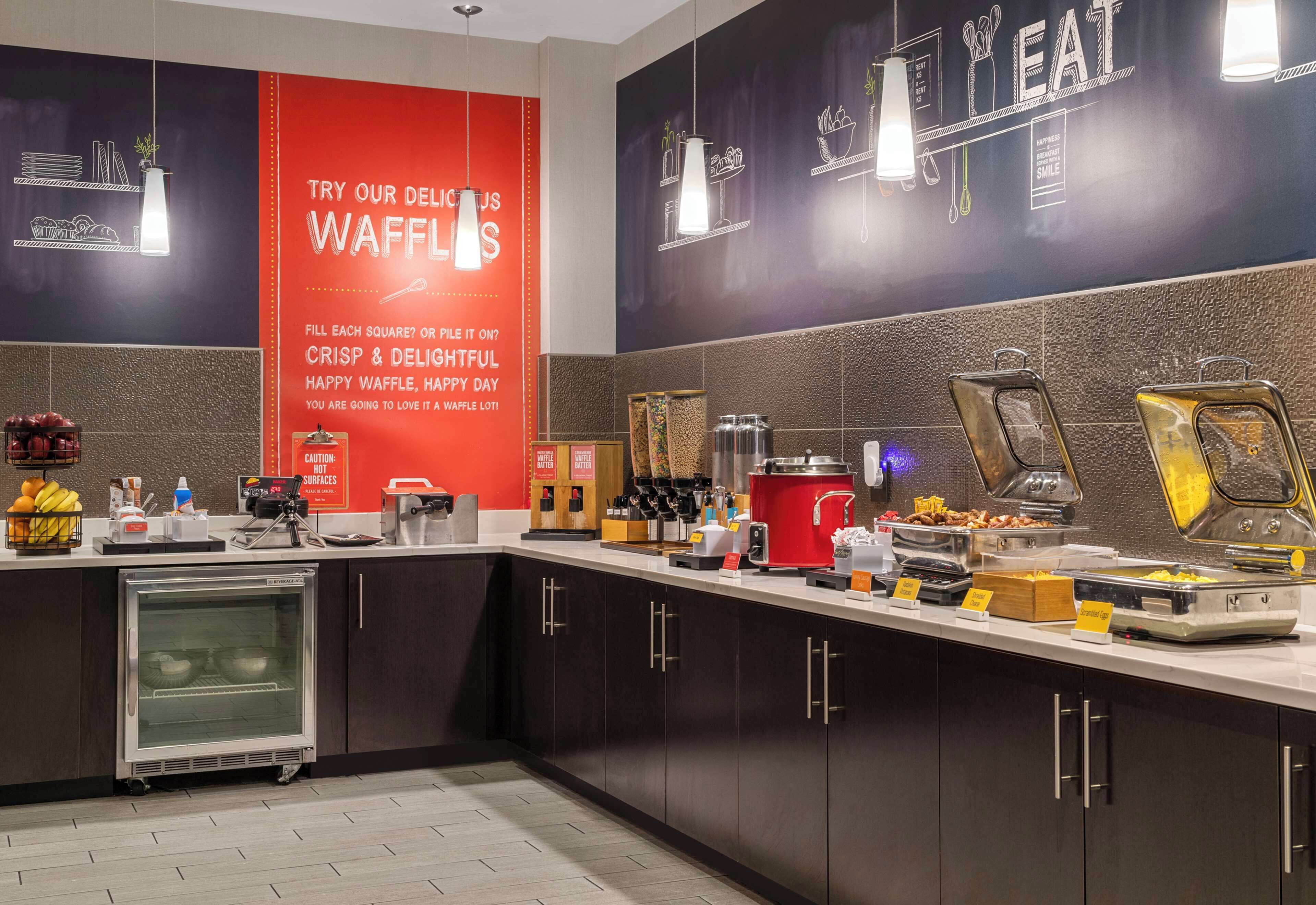 A buffet area with a red banner advertising waffles, various food stations, and a refrigerator.