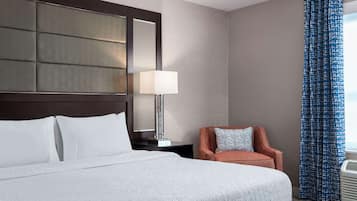 Een hotelkamer met een groot bed, een nachtkastje met lamp, een stoel en een raam met gordijnen.