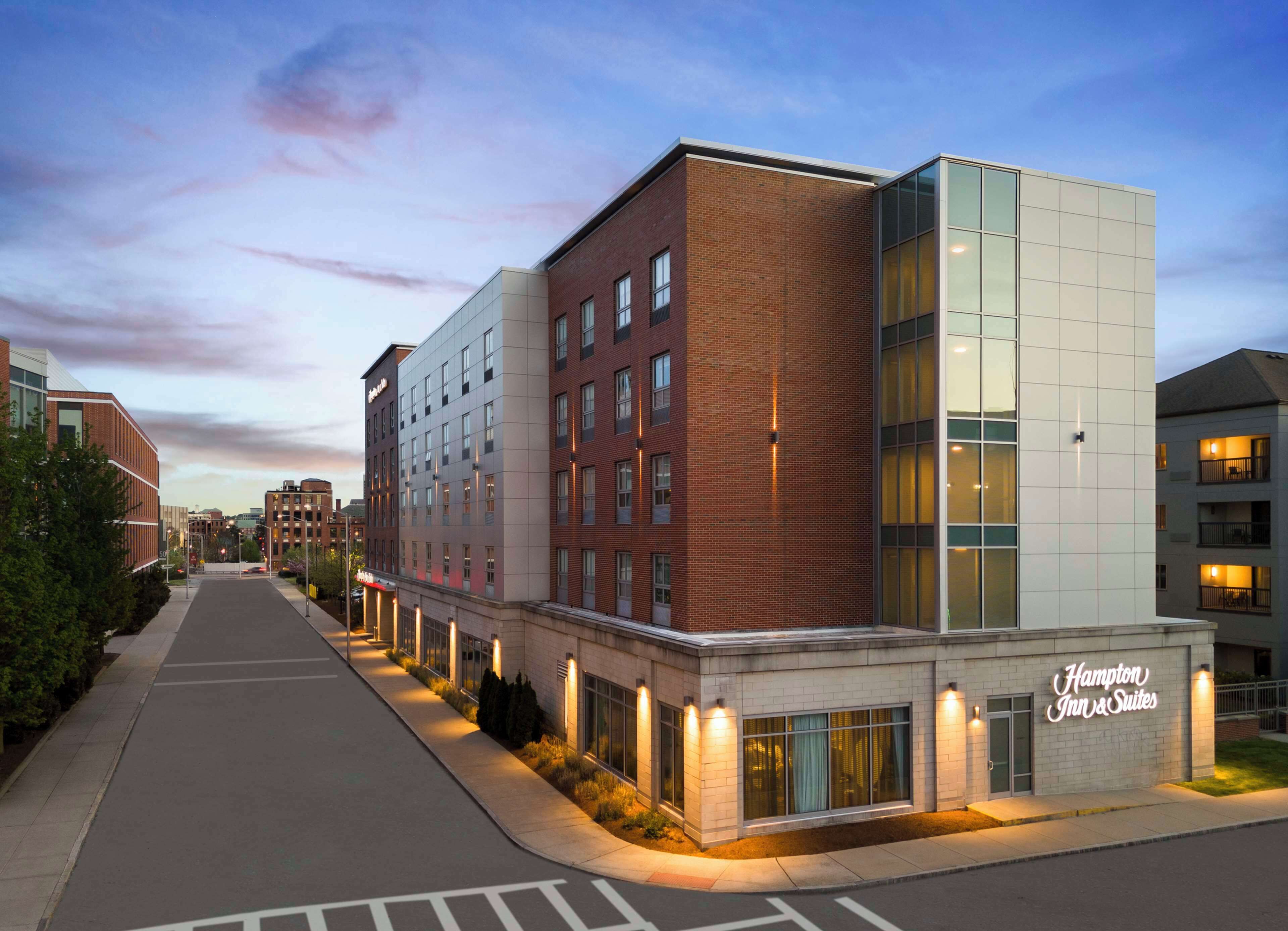 Ein modernes Gebäude mit Back- und Glasfassade, das ein gut sichtbares Hampton Inn & Suites Schild zeigt.