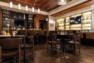Un espace bar doté d’un plancher en bois, de tabourets de bar et de diverses bouteilles et verres disposés sur des étagères.