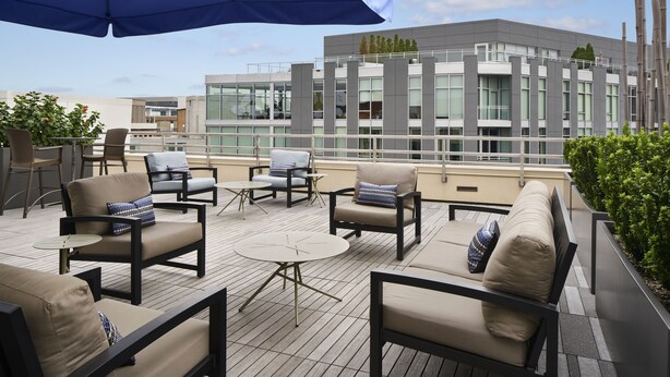 A rooftop terrace with outdoor seating, including sofas and chairs, and a large umbrella providing shade. - Hyatt Place Washington DC/Georgetown/West End (Washington)