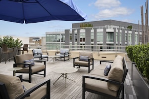 A rooftop terrace with outdoor seating, including sofas and chairs, and a large umbrella providing shade.