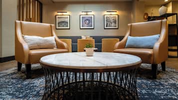 A modern lounge area with leather armchairs, a round table, and framed artwork on the wall.