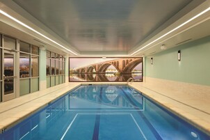 An indoor swimming pool with clear blue water, a mural of a bridge on the wall, and a tiled floor.