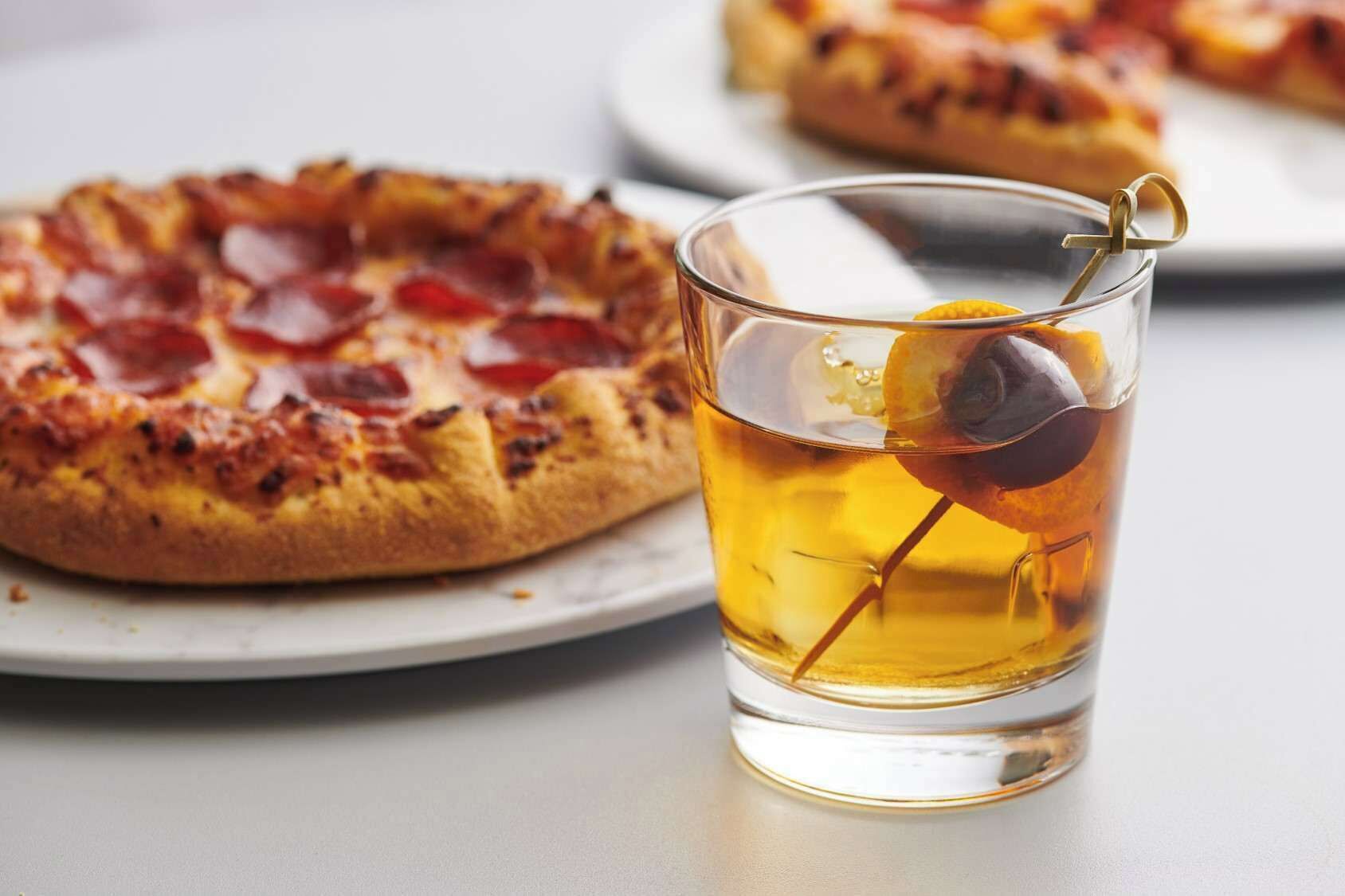 Pizza con pepperoni y un vaso de bebida de color ámbar adornado con aceitunas.