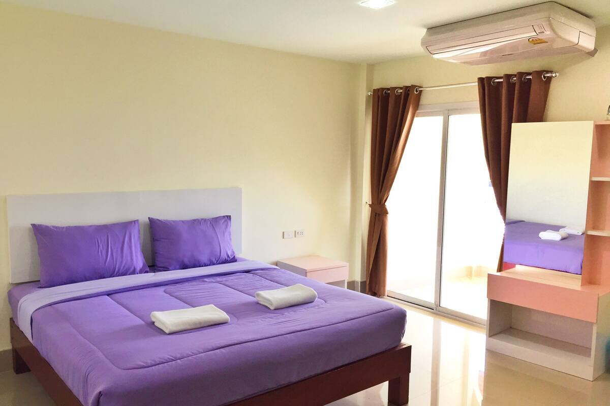 Un dormitorio con cama, mesita de noche, espejo y ventana con cortinas.