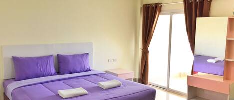 A bedroom with a bed, a nightstand, a mirror, and a window with curtains.