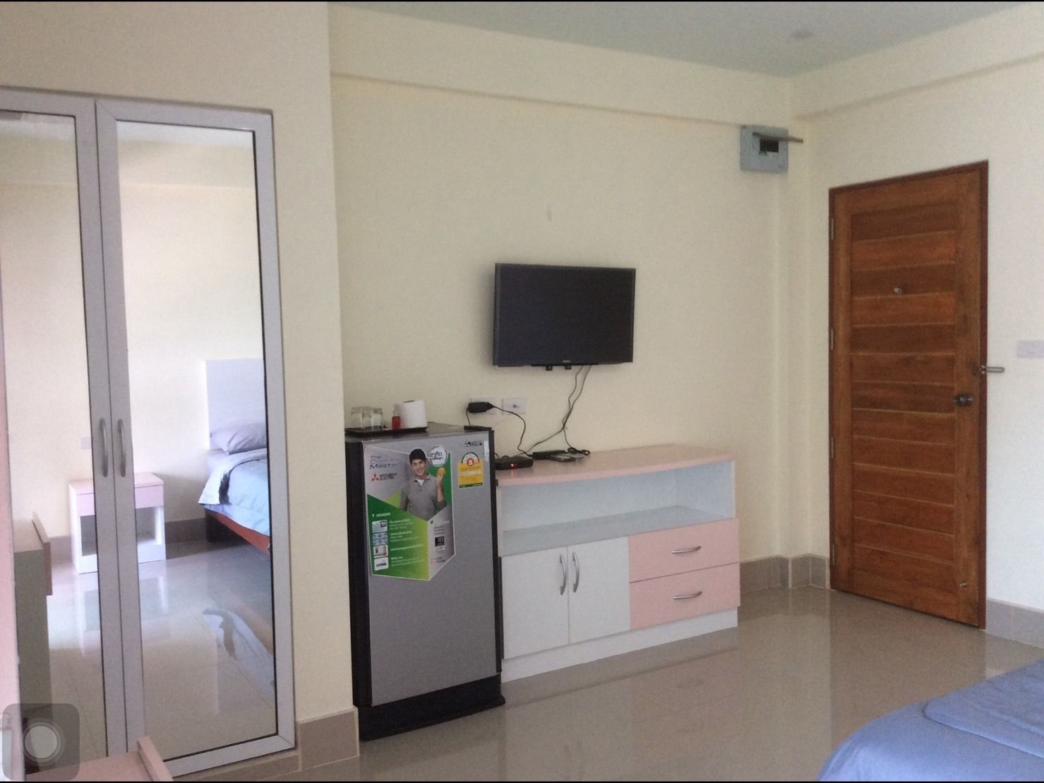 Un dormitorio con cama, armario, escritorio y televisor, además de una puerta.