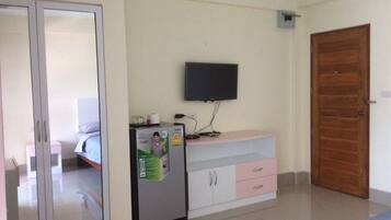 Un dormitorio con cama, armario, escritorio y televisor, además de una puerta.