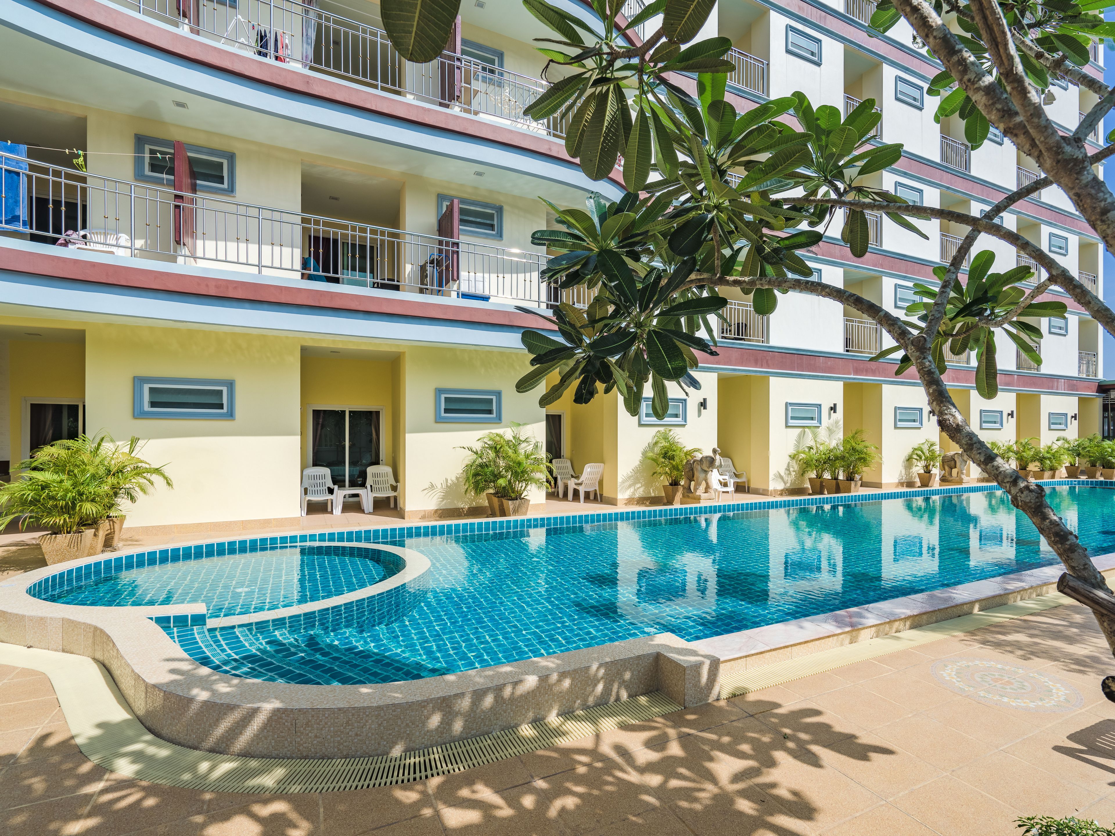 A hotel with a swimming pool, multiple balconies, and potted plants.