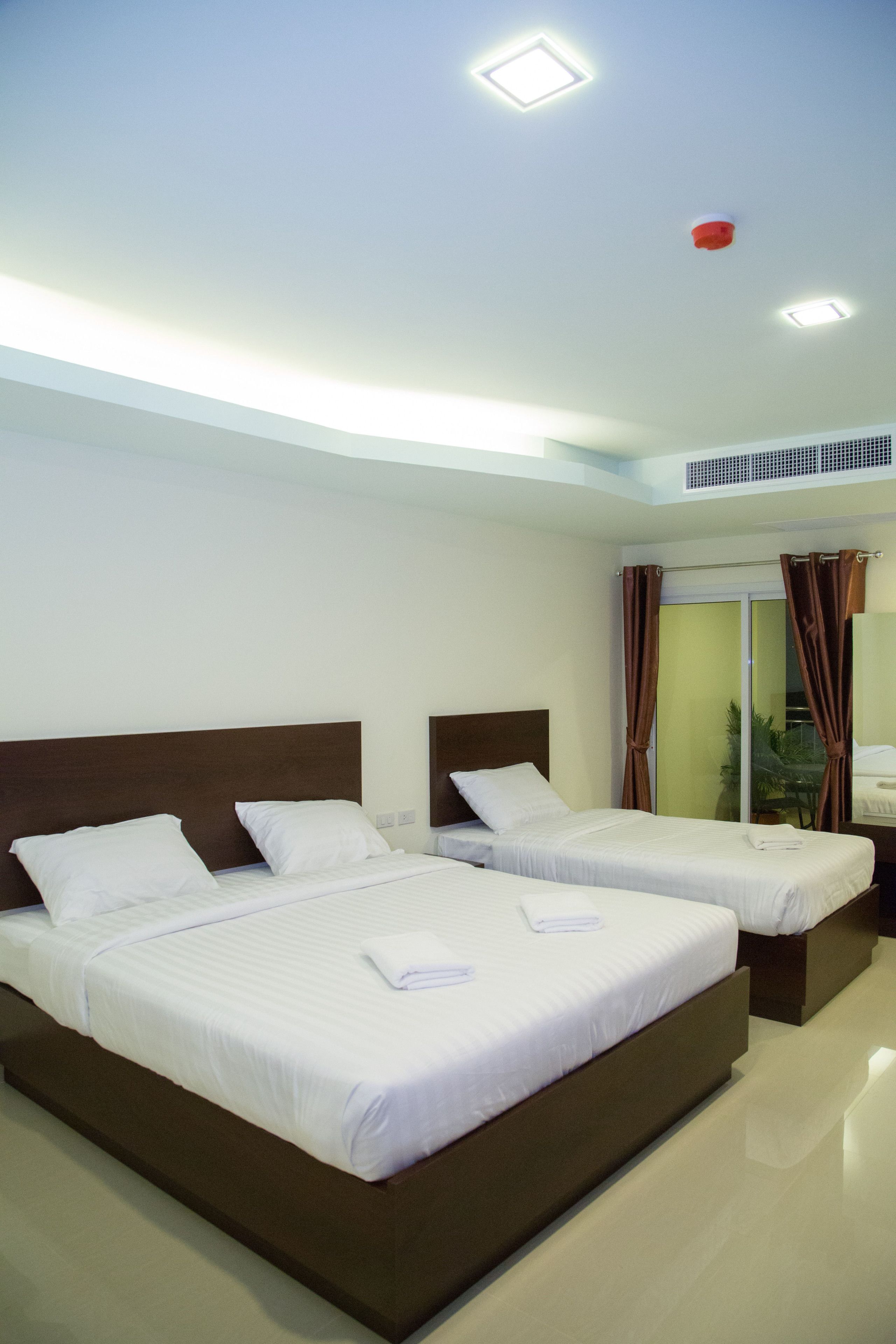 A hotel room with two beds, a large window with curtains, a ceiling fan, and a visible air conditioning unit.